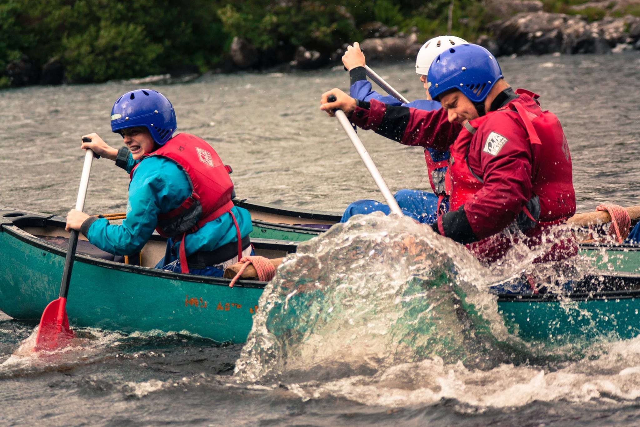 3 Boys Brigade Members out on the water in a kayak. The rear left member is mid stroke with a huge wave of water following his pedal.