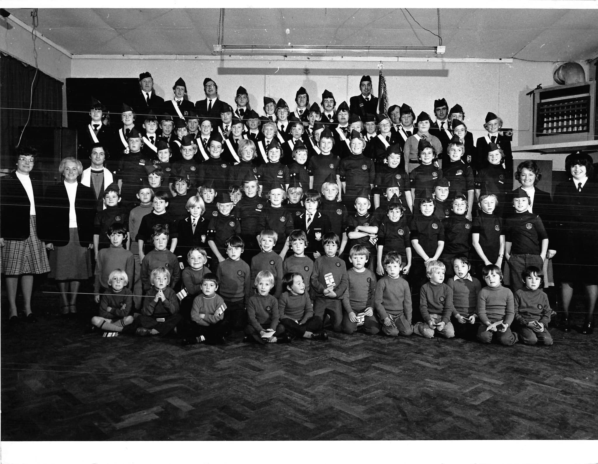 A black and white photo showing a gathering of Boys Brigade Members of all ages, They line up behind each other forming rows across the hall, the rows go from youngest members to oldest.